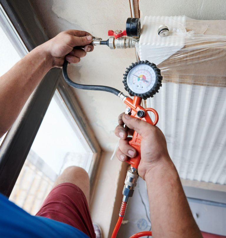 Plumber filling pipes with pressurized air to inspect for leaks in new heating system installation.